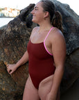 JAYD athlete Kim Doyle wearing the Airlie one piece in cinnamon with contrasting fairy floss shoulder straps, standing next to a rock and gazing off into the distance.
