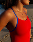 The JAYD swimwear Airlie one piece Ruby swimsuit glowing on model Pipi in the morning sun, with bold cobalt blue shoulder straps contrasting vividly against the red.