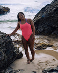 JAYD Swimwear athlete Sara leaning on a rock at the beach wearing the Airlie Vibe one piece with contrasting lilac haze straps.