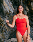 Ski paddler Jenaya Massie leaning against a rock at the beach wearing the JAYD Swimwear Airlie one piece swimsuit.