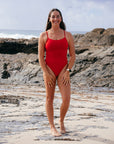 JAYD athlete Jenaya Massie standing on a beach wearing the Airlie one piece in Ruby red.