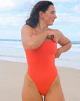 Open water swimmer Madi wearing the Albi one piece in Blaze red, standing on a beach gazing into the distance.