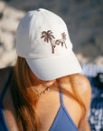 JAYD model sitting on a beach wearing the cream JAYD Swimwear baseball cap.