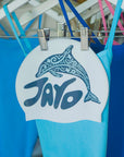 White swim cap with dolphin design and 'JAYD' branding hanging on a rack of complimentary blue JAYD one piece swimsuits.