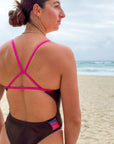 JAYD Swimwear athlete Jenaya Massie wearing the Lennox one piece swimsuit in cacao with contrasting orchid fixed-back straps and multi-coloured hip cut-outs.