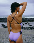 The Ibiza piece swimsuit by JAYD Swimwear in varying shades of lilac haze and acai purple. The contrasting acai cross over shoulder straps and hip cut-outs stand out against the light purple lilac haze full bum coverage swimsuit body.