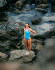 JAYD Swimwear model Molly standing next to a rock pool wearing the JAYD Ibiza one piece swimsuit in nautical mykonos and cobalt contrasting shades.