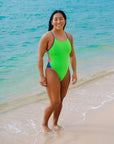 Surf life saving athlete Sara standing on a beach wearing the Splice fluro green x Storm blue Ibiza one piece swimsuit.