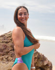 Ski Paddler Jenaya Massie on the beach wearing the JAYD Swimwear Ibiza One Piece in Atlantic with Lilac Haze straps & contrasting hip cut-outs.