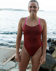 Athlete Lizzie Welborn standing in front of the open water wearing the JAYD swimwear Ibiza One Piece in Cinnamon with contrasting Pink Sorbet straps.