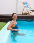 Side view of model in a pool wearing the Airlie One Piece Athletic Swimsuit in Nordic Blue by JAYD Swimwear.