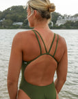 Close back view of a female athlete wearing a JAYD Swimwear one piece swimsuit, Apsley in Olive green, standing on a beach.