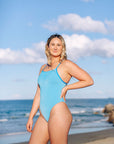 Woman wearing JAYD Albi one piece swimsuit in Waikiki blue with contrasting Cancun cross back straps on the beach