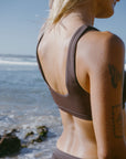 Woman in a brown JAYD Swimwear bikini top, Nalu in Cacao, standing by the beach.