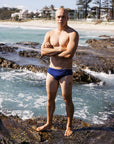 Ocean athlete Tanner wears the chlorine-resistant Ramshark men’s swim bottom in Navy by JAYD Swimwear. Front view showcasing the sleek, performance-ready fit.
