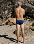 Back profile of ocean athlete Tanner wearing the Navy Ramshark men’s swim bottom by JAYD Swimwear. Chlorine-resistant and designed for performance, movement, and durability in the water.