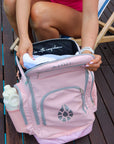 Model opening the top compartment of the pale pink JAYD Swimwear Backpack.