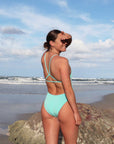 JAYD Swimwear, athletic one piece, tallow in Sea Mist colour. Looking back over shoulder on the beach.