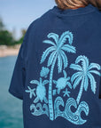 Back view of a model wearing JAYD Swimwear's navy oversized tee with a light blue turtle and palm tree graphic, styled for a post-swim, beach lifestyle.