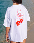 Back view of a model in JAYD Swimwear's white oversized tee, printed with a red disco-ball cherry graphic and Mon Cheri text.