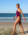 Athlete Lucy walking down the beach in her favourite Sangria JAYD Swimwear one piece, showcasing the high-cut hip cut which elongates the legs.