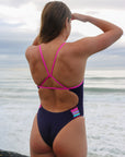 Back view of model on a rock wearing JAYD Swimwear athletic one piece, Lennox, in Acai Purple.