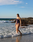 Side view of model in the shallows wearing JAYD Swimwear athletic Airlie one piece in Acai.