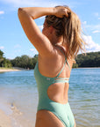 Rear standing view of JAYD Swimwear's full-coverage athletic one-piece Airlie in the shade Matcha.