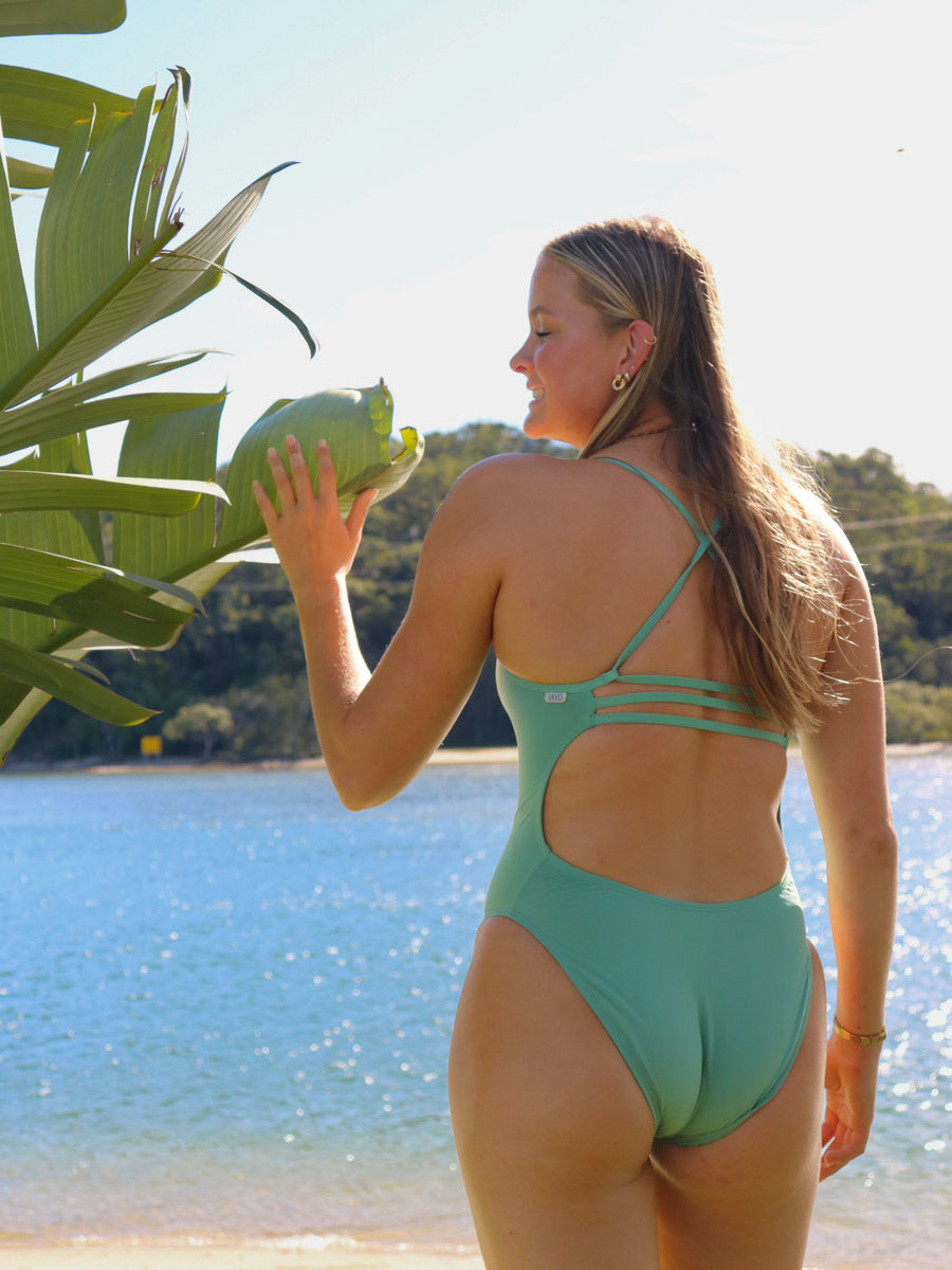 Rear standing view of JAYD Swimwear's full-coverage athletic one-piece Airlie in the shade Matcha.