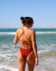 Back view of model walking on a beach wearing JAYD Swimwear athletic one piece Isla in Cinnamon.