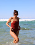 Front view of model walking in the water wearing JAYD Swimwear athletic one piece Isla in Cinnamon.