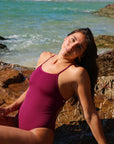 Front view of model on a rock wearing JAYD Swimwear athletic one piece Tallow in Sangria.