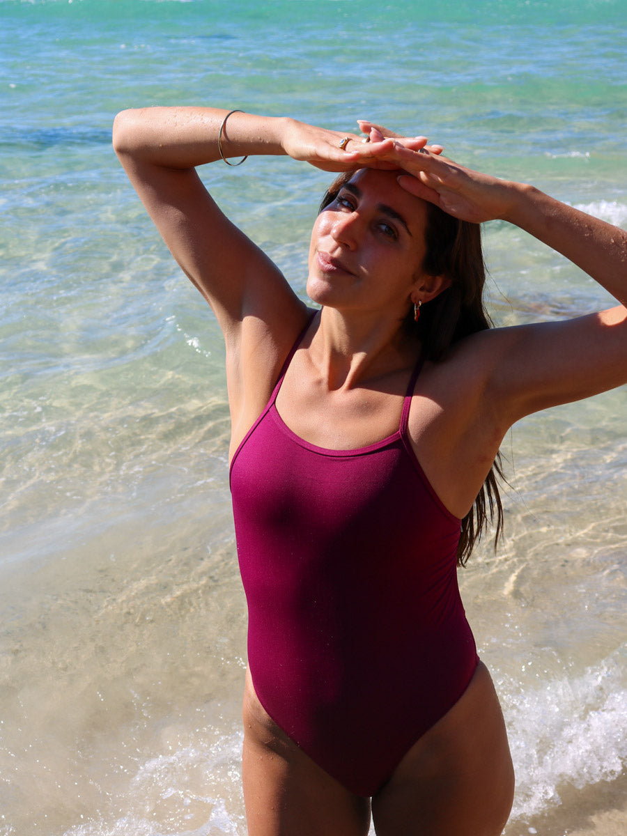 Front view of model on a beach wearing JAYD Swimwear athletic one piece Tallow in Sangria.