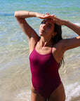 Front view of model on a beach wearing JAYD Swimwear athletic one piece Tallow in Sangria.