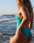 Side view of model on a beach wearing JAYD Swimwear athletic one piece Tallow in Atlantic