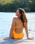 Back view of JAYD Swimwear's full-coverage athletic one-piece Tallow in Sunshine. Model is seated.