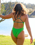 Back view of model walking on grass wearing JAYD Swimwear athletic one piece swimsuit Zambia in Moss Green.