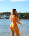 Back view of model on beach wearing JAYD Swimwear athletic one piece Zambia in Neon Orange.