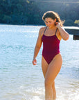Front view of model on beach wearing JAYD Swimwear athletic one piece Zambia in Sangria.