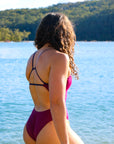 Side view of model on beach wearing JAYD Swimwear athletic one piece Zambia in Sangria.