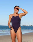 Close front view of model on a beach wearing JAYD Swimwear cheeky one piece Zimmy in Acai.