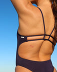 Close back strap view of model in the sun wearing JAYD Swimwear cheeky one piece Zimmy in Acai.