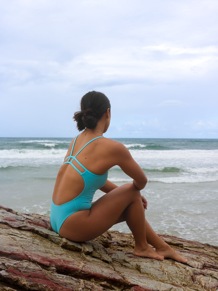 Back view of model on the beach wearing JAYD Swimwear athletic Zimmy one piece in colour shade Mykonos blue.