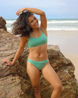 Front view of model wearing athletic, cheeky coverage JAYD Swimwear Minnie bikini bottoms in matcha green.