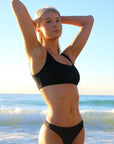 Front view of model on a beach wearing JAYD Swimwear athletic bikini top Nalu in Black.