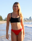 Front view of model on a beach wearing JAYD Swimwear athletic bikini top Torquay in Black.