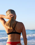 Back view of model on a beach wearing JAYD Swimwear athletic bikini top Torquay in Black.