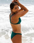 Close side view of female swimmer, Carla Papac, in Cove Tazzie JAYD Swimwear bikini top standing on a beach with ocean waves in the background.