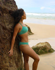 Side view of model leaning against a rock wearing JAYD Swimwear athletic Torquay training bikini top in Matcha green.