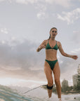 Model surfing in JAYD Swimwear Cali athletic bikini bottoms in Matcha Green by JAYD Swimwear